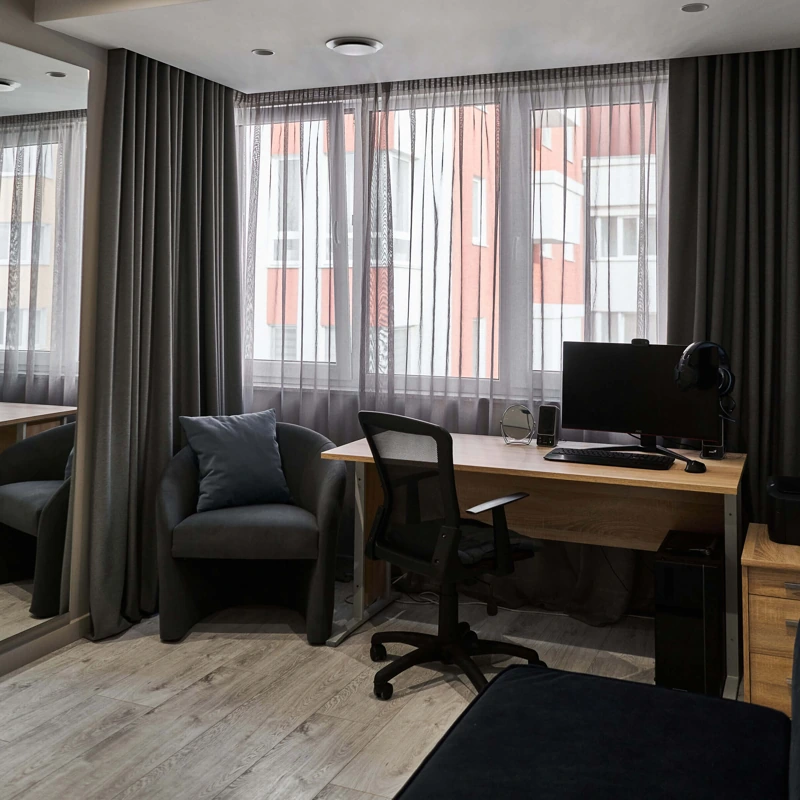 Home office with desk, gray curtains, and window.