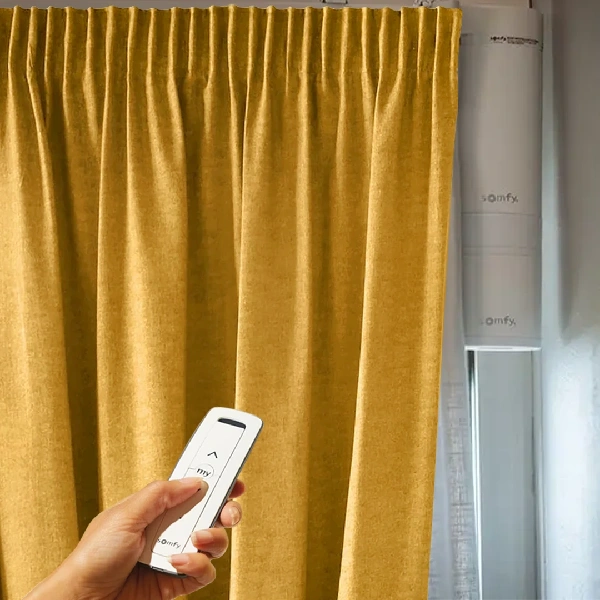 remote control in front of a golden yellow pencil pleat curtain.